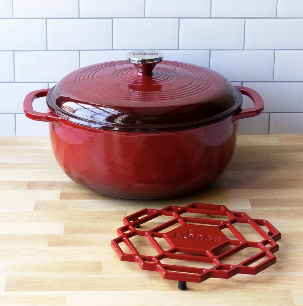 The red cast iron round dish with lid and matching red pot rest next to it