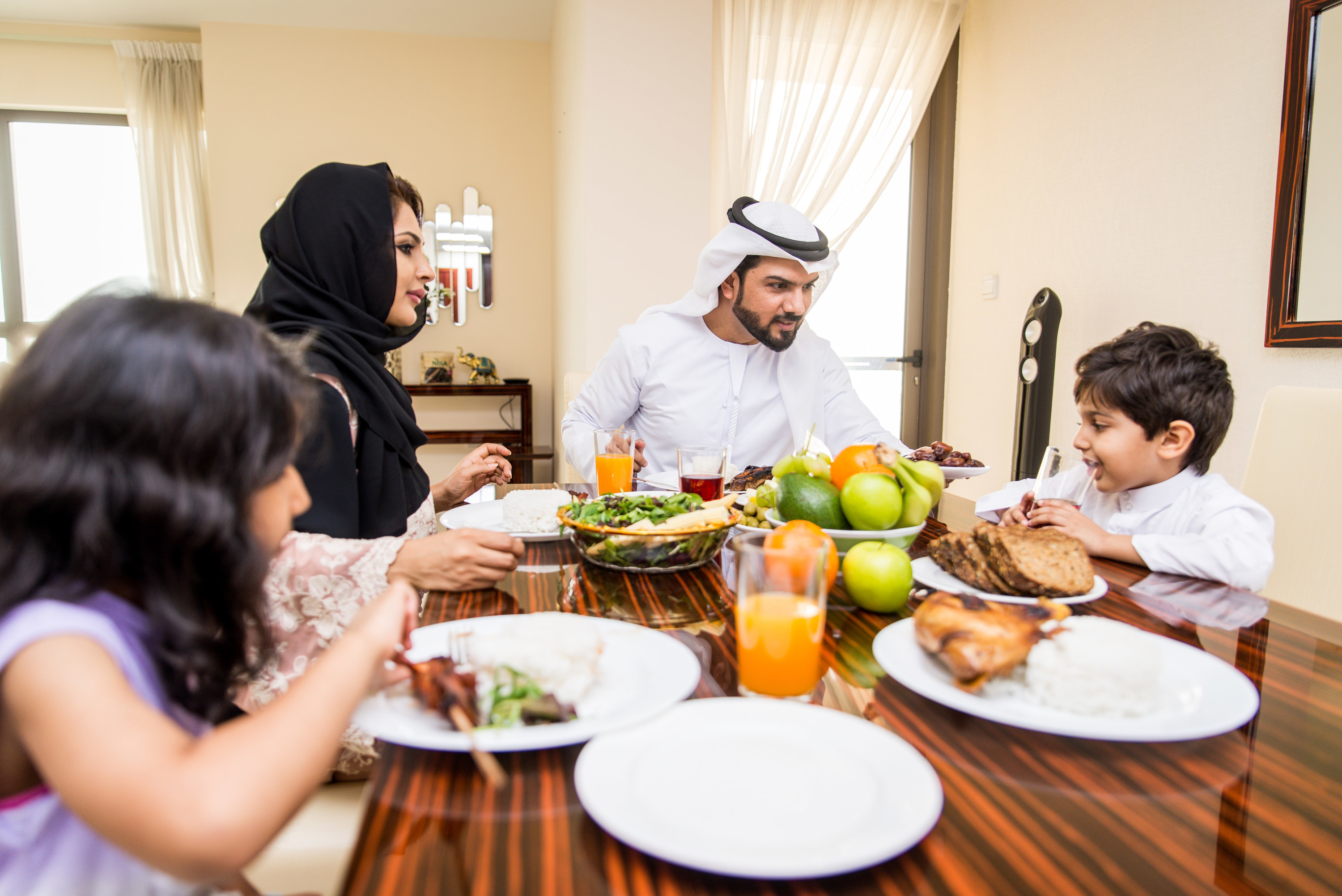 arabic family enjoying dinner together at a rectangular shiny wooden table