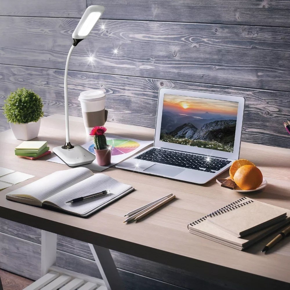 A desktop with the lamp, a laptop, notebooks, assorted pens, an orange on a plate, a cactus, a coffee and a small shrub with sparkle illustration the disinfecting action