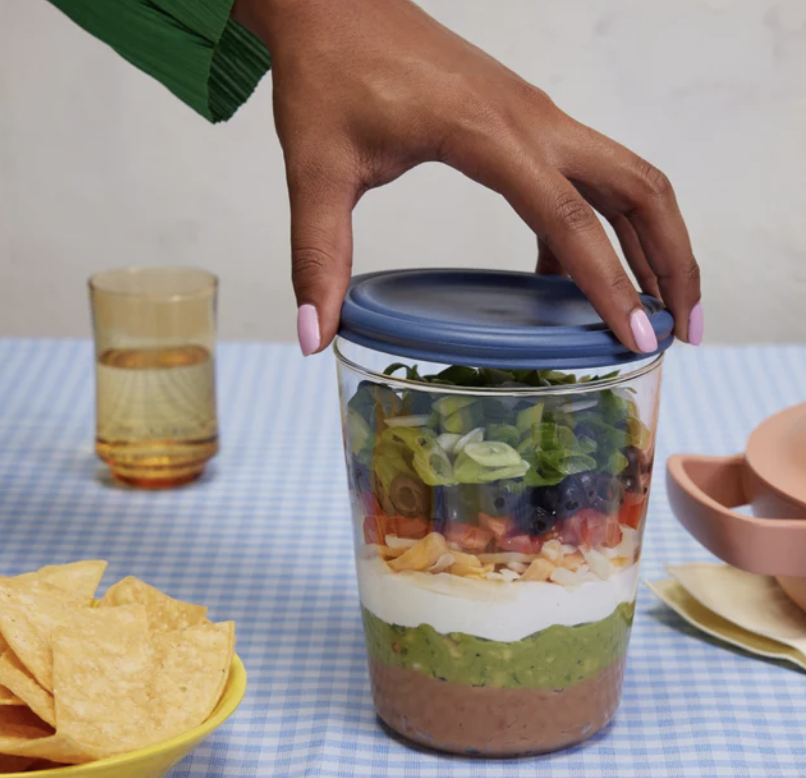 A person putting a lid on a container filled with seven layer dip