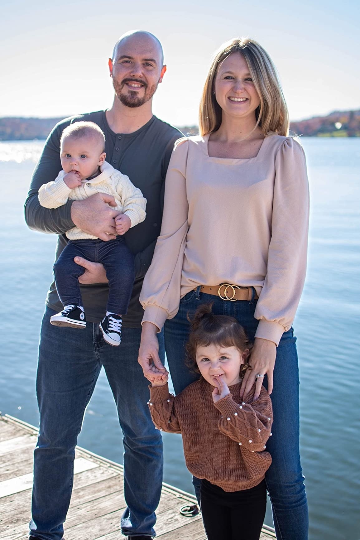 A reviewer wearing the cream top in a family photo with jeans, a little kid in brown and black, a reviewer in a grey top and jeans holding a baby in cream and denim