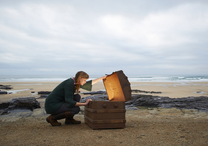 A young girl looking in a chest with light coming out of it