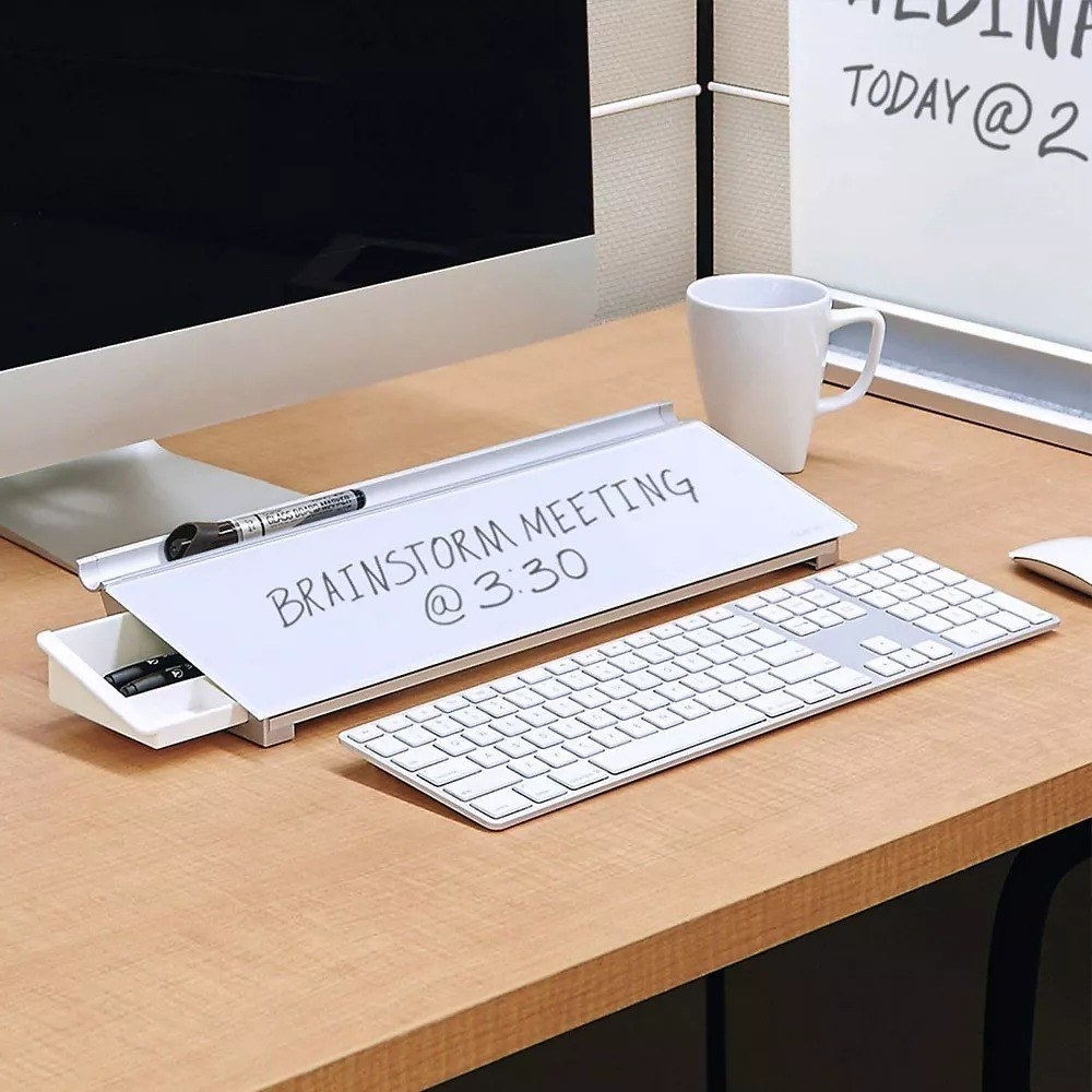 A desk with the glass dry-erase board displaying a hand-written memo that reads &quot;brainstorm meeting at 3:30&quot;