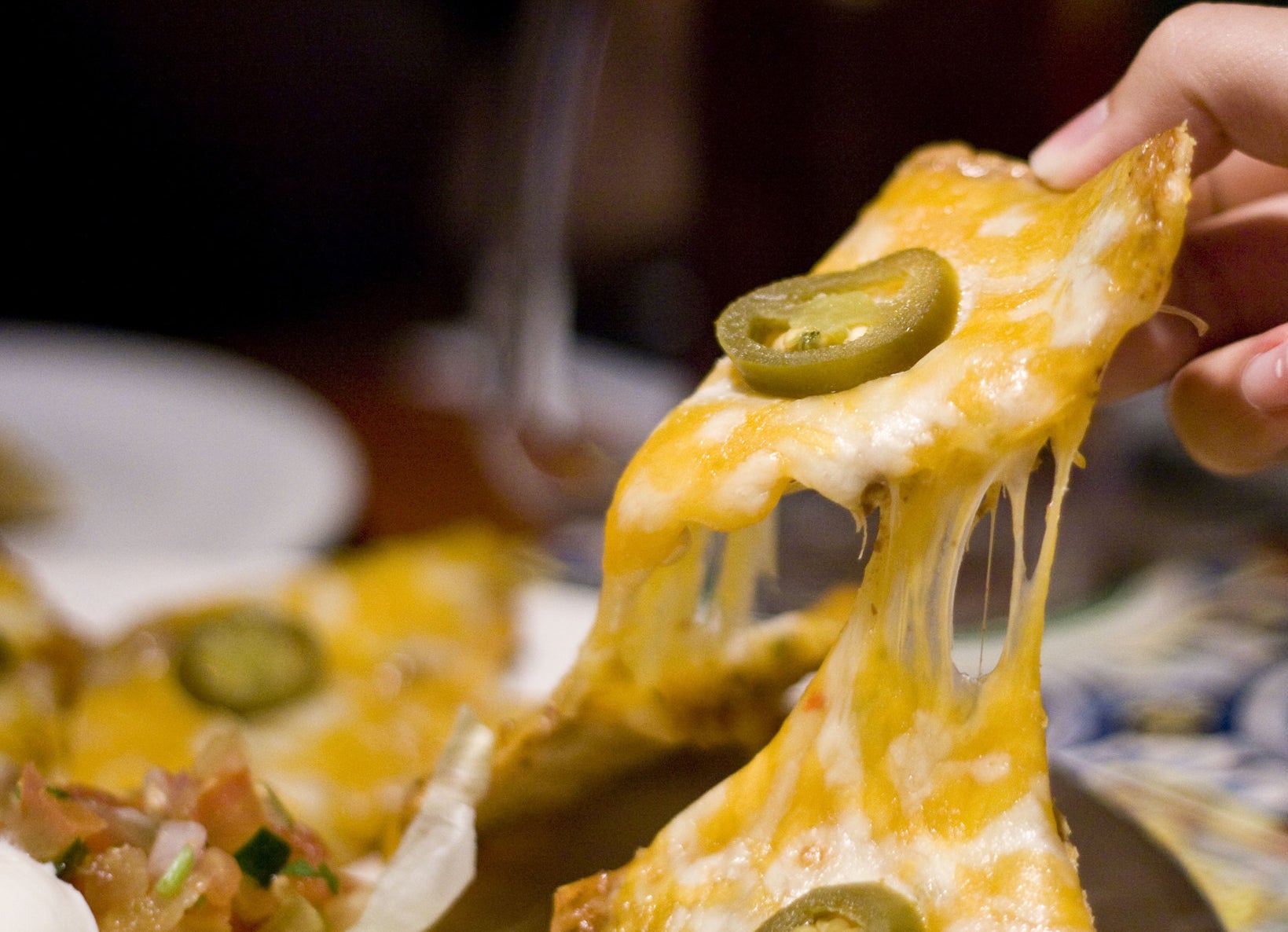 Hand holding cheesy cheese nachos.