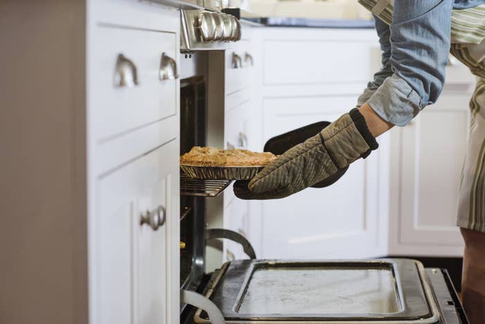 hands putting a pie into the oven