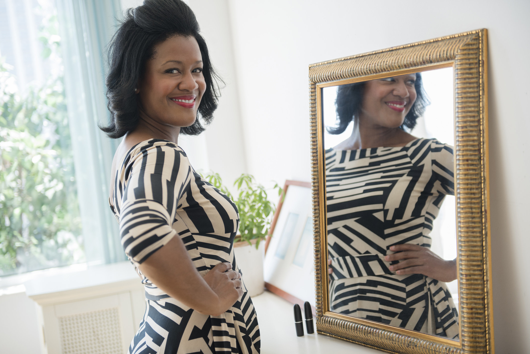 Smiling woman standing in front of a mirror and wearing a dress