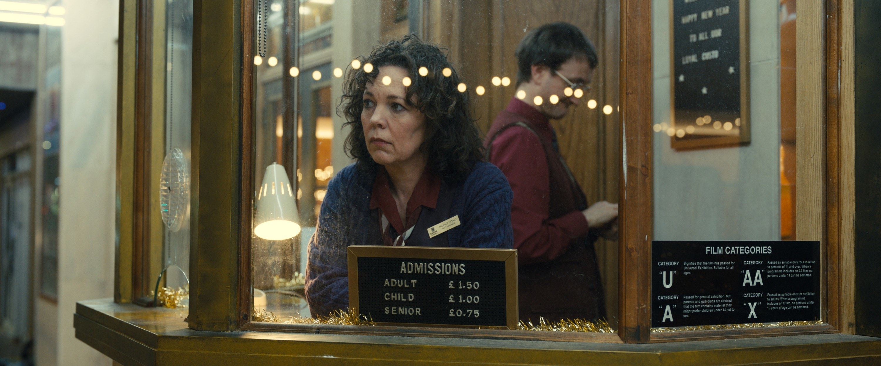 Olivia Colman sits in a ticket booth