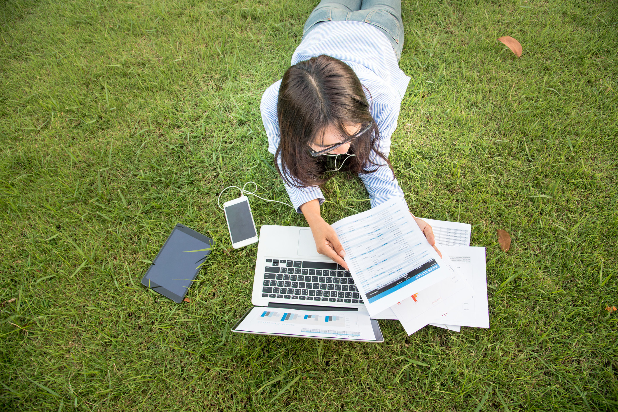 A woman lying on the grass working on a laptop