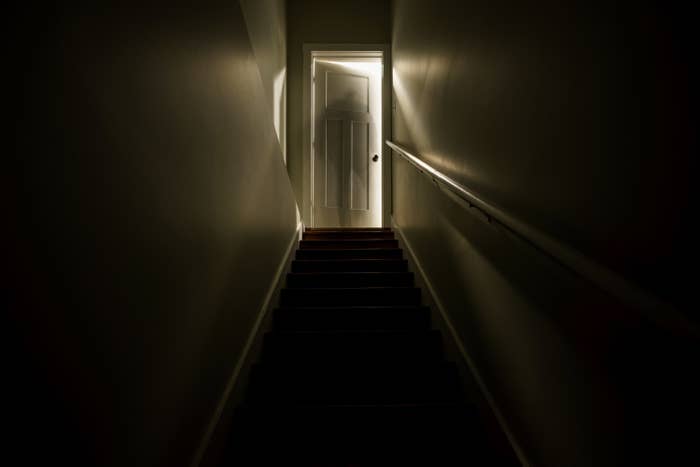 A dark stairwell illuminated by a slightly opened door at the top of the stairs
