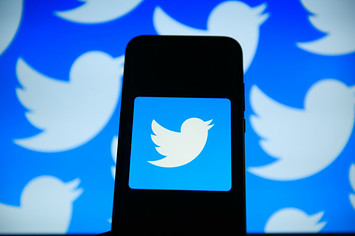 Twitter logo is seen on an android mobile phone in front of a computer screen
