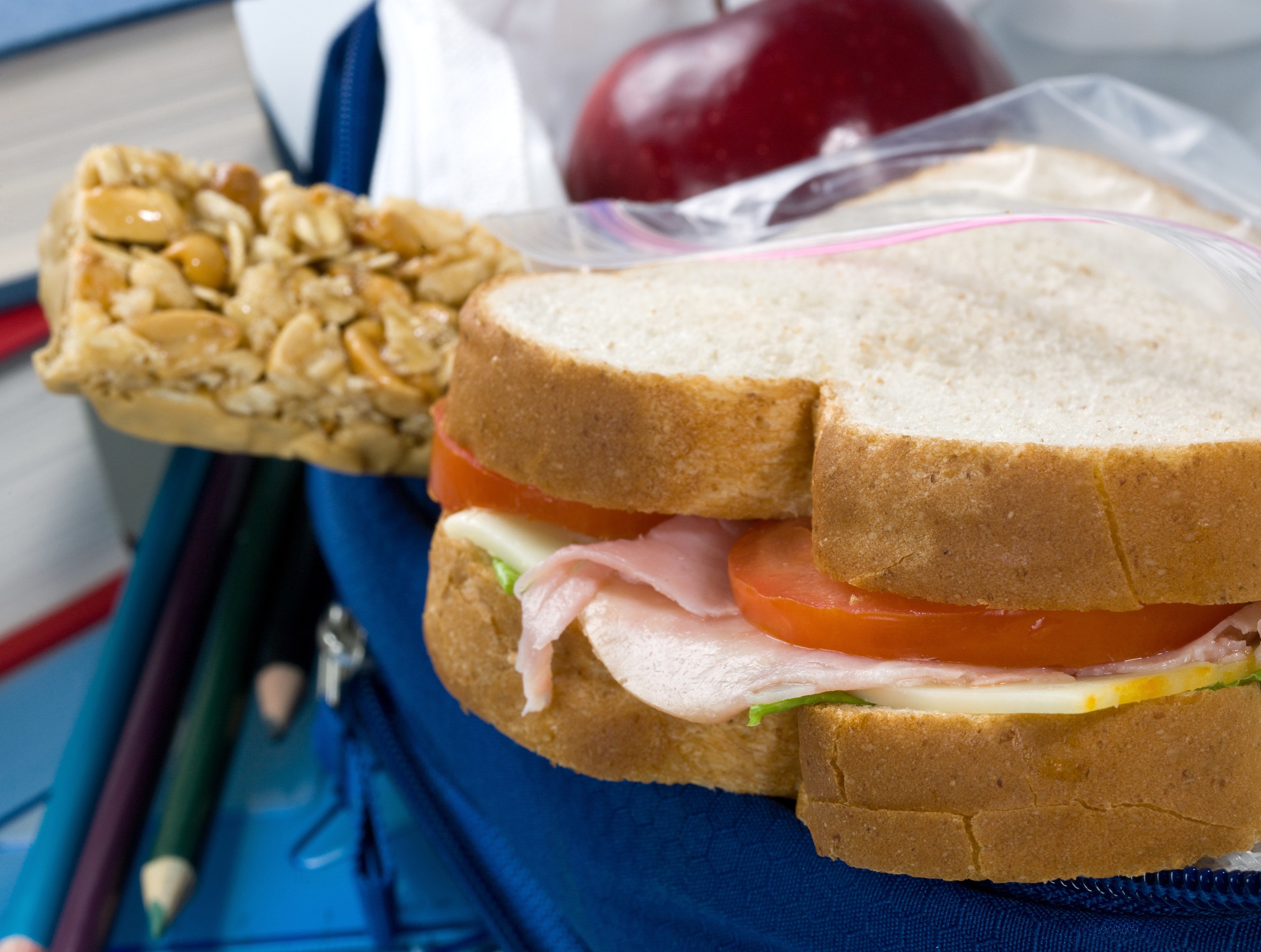 a sandwich and a granola bar with an apple in the background