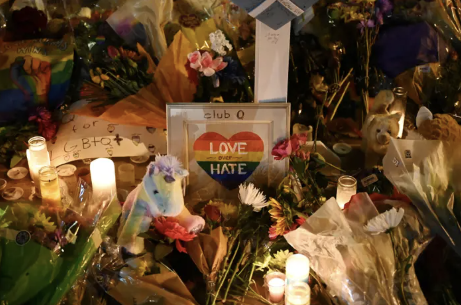 A memorial with flowers and candles and a small photo frame that says &quot;love over hate&quot; in a rainbow heart