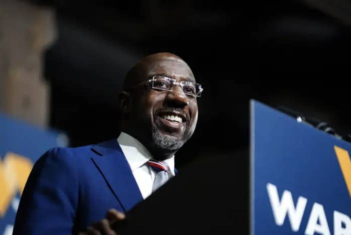 Sen. Raphael Warnock speaks in front of a podium during a rally