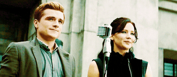 Peeta and Katniss stand in front of a microphone