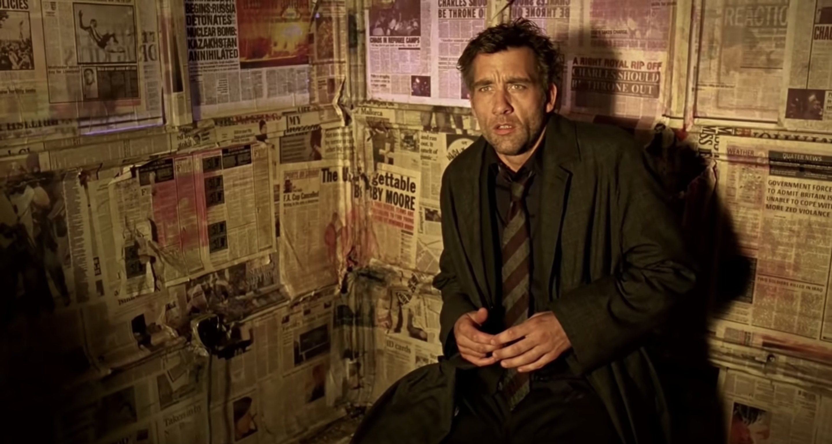 Clive Owen in a room plastered with newspapers
