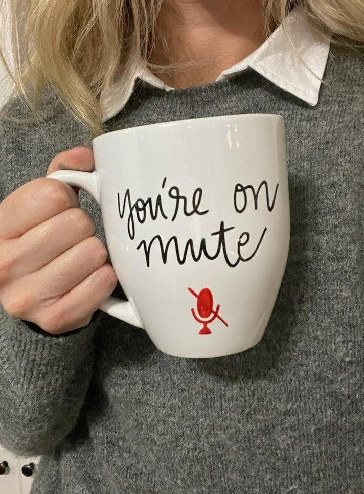 a model holding a white mug with cursive script that reads &quot;You&#x27;re on mute&quot;