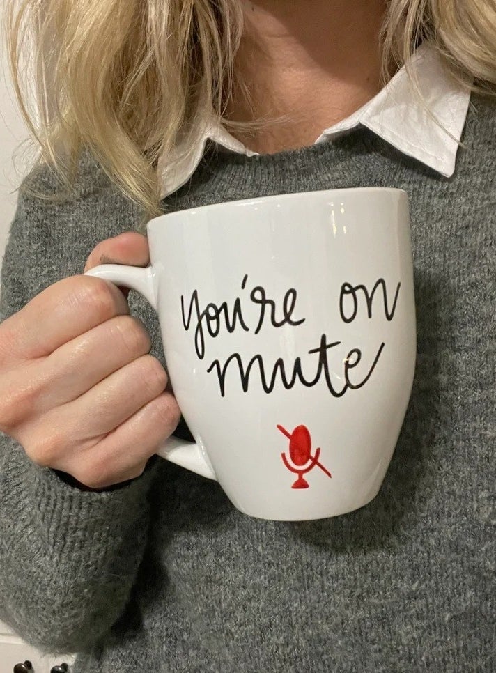 a model holding a white mug with cursive script that reads &quot;You&#x27;re on mute&quot;
