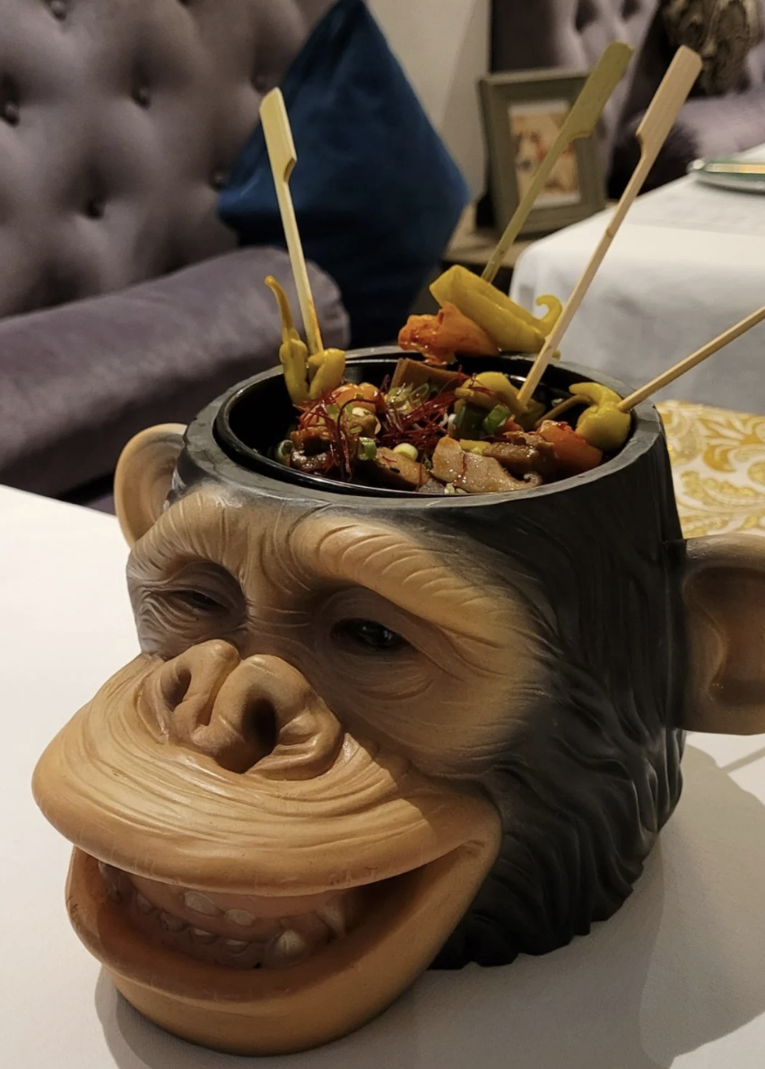 A monkey head with the top cut off and a bowl of food placed where the brain would be