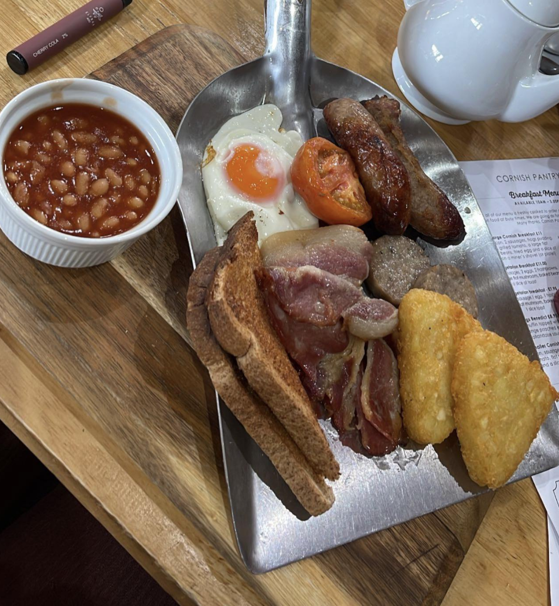 A large breakfast, with eggs, beans, toast, hash browns, ham, and sausage served on the scooper end of a shovel