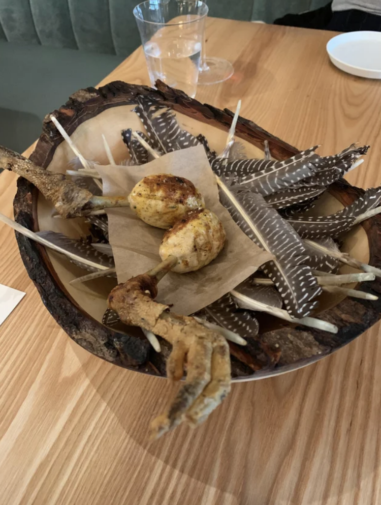 Two drumsticks served in a bowl on top of a bed of real feathers