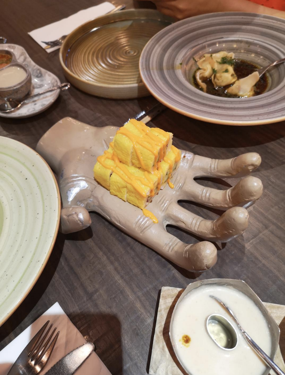 A creepy looking larger than normal fake hand holding what appears to be sushi rolls