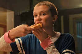 Eleven from Stranger Things eating a slice of pizza