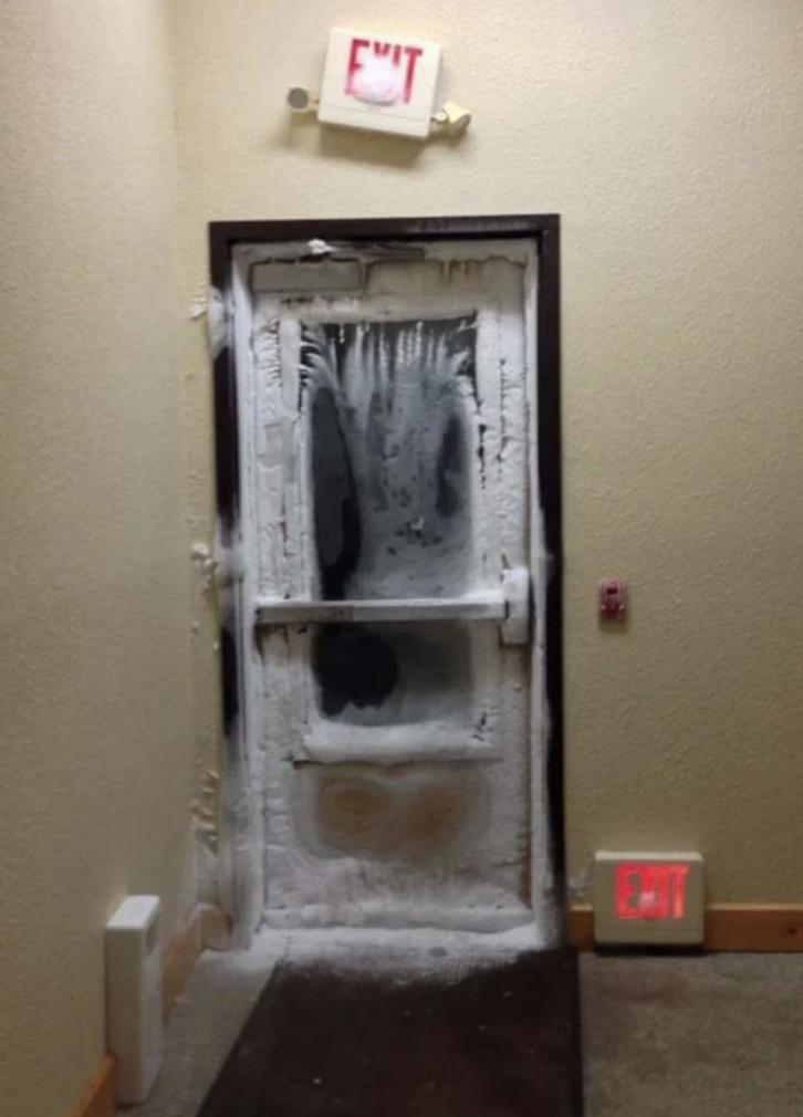 A door with an exit sign above it covered in snow and ice