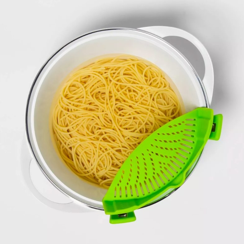 Green strainer attached to a pot with spaghetti in it