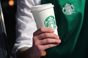 An employee holds a paper cup at the Starbucks drive thru cafe.