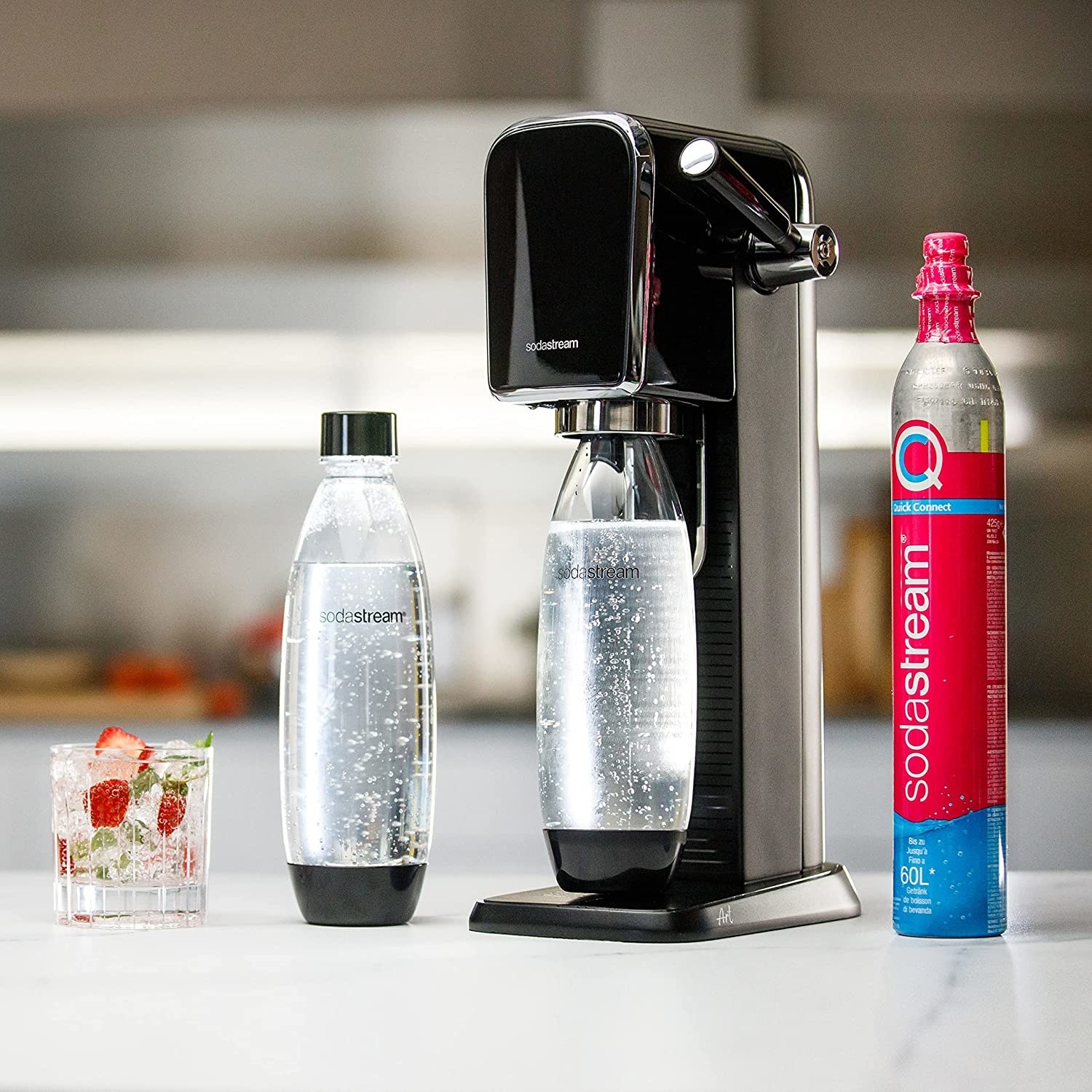 a soda stream next to two bottles, a glass, and a co2 canister