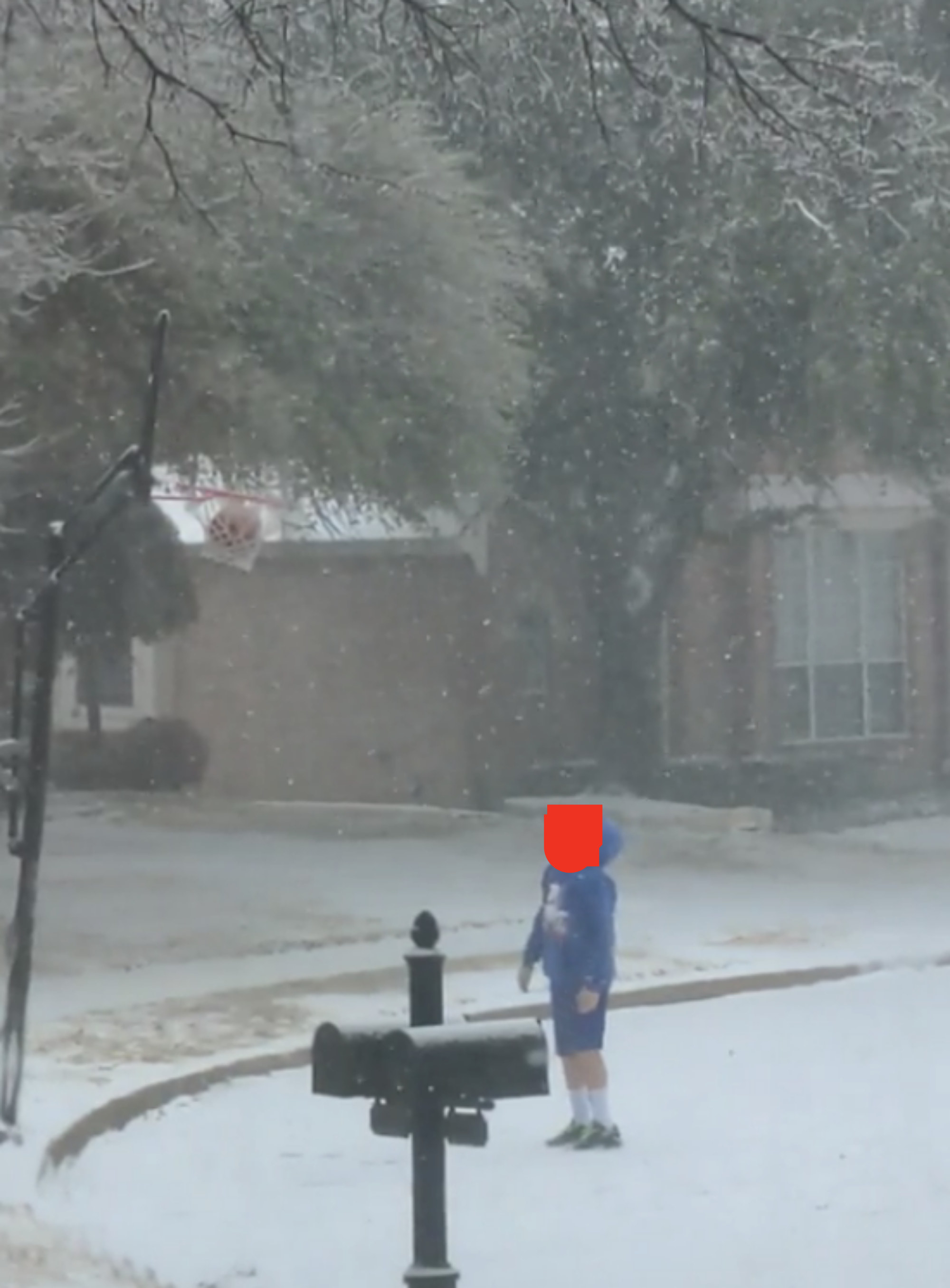Kid looking up at a basketball stuck in a hoop on a snowy street