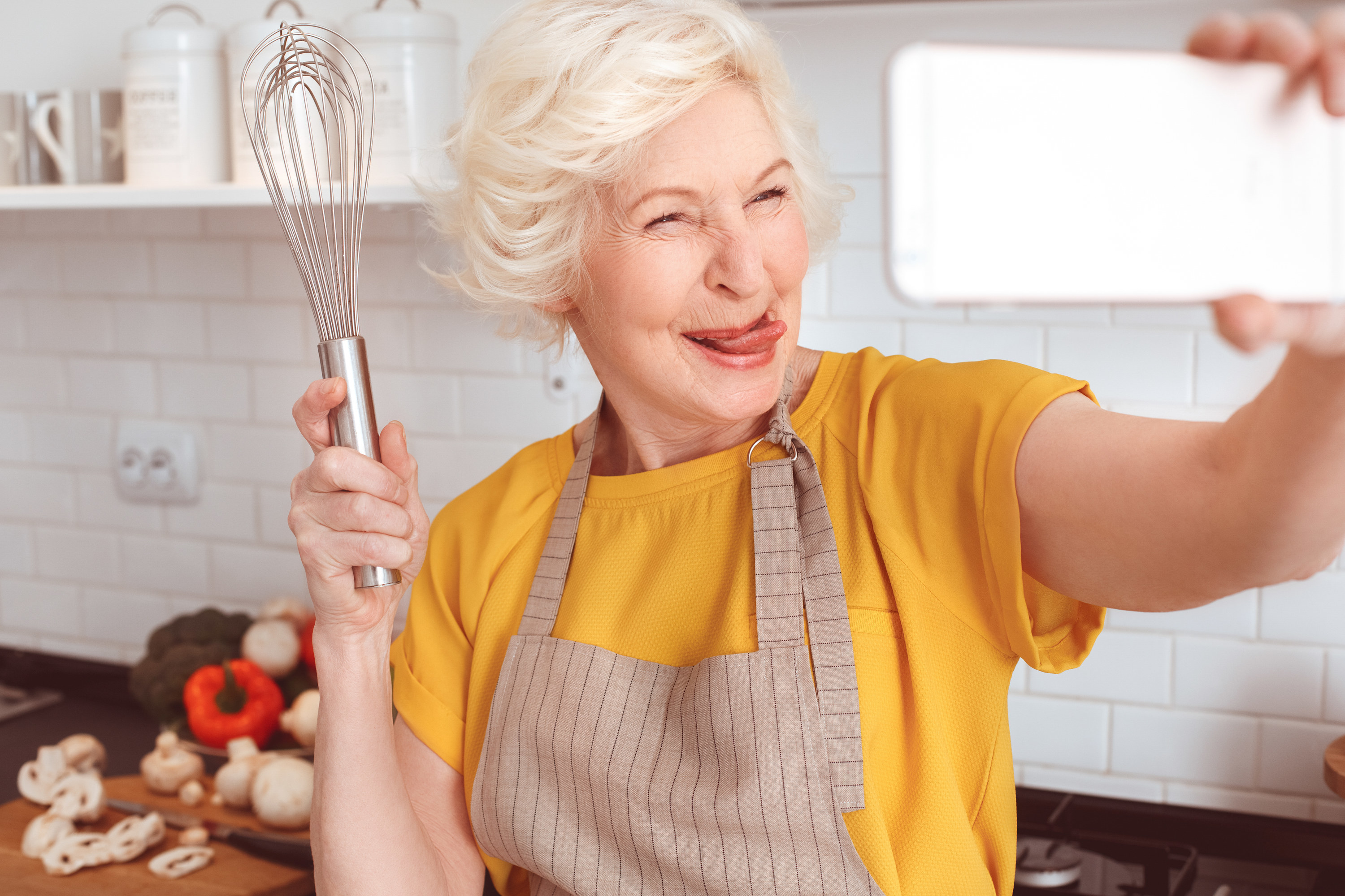 a woman in the kitchen taking a selfie with her whisk