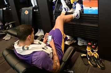 Kyle Kuzma sits at his locker on his phone.