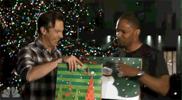 Two men excitedly opening gift bags in front of a Christmas tree