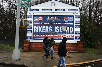 People walk by a sign at the entrance to Rikers Island