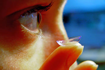 A woman demonstrates putting a contact lense in.