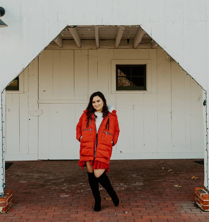 A reviewer wearing a red coat with black boots and a white top