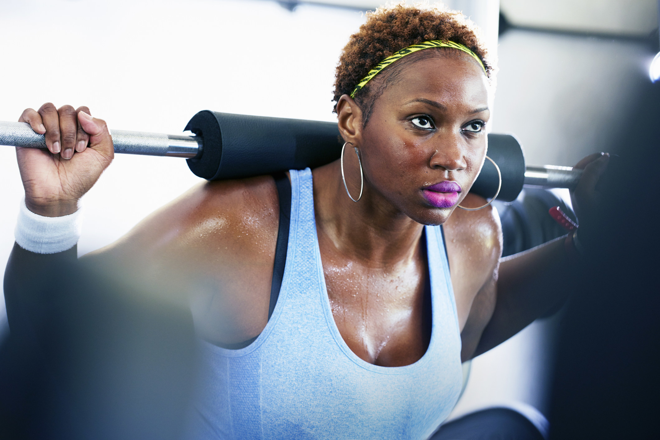 A woman stands with a weight bar on her back