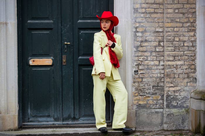 Emma Friedsell wearing a yellow suit, red cowboy hat, scarf, and bag outside Stine Goya