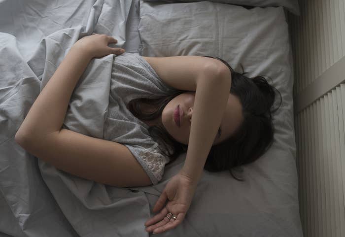 a woman lying in bed with her arm over her eyes