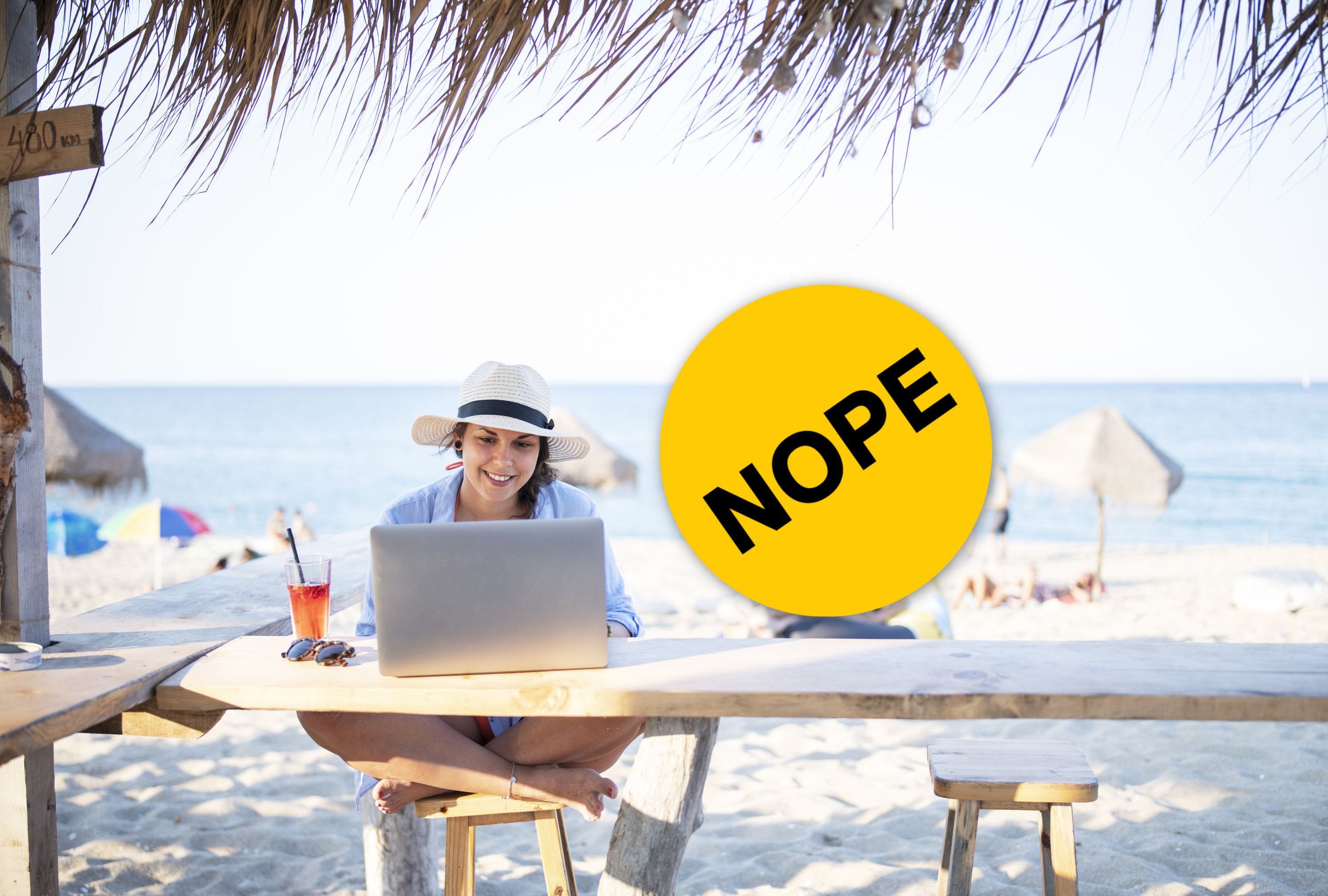 woman working on a laptop while on a beach vacation with a nope sticker overlay beside her