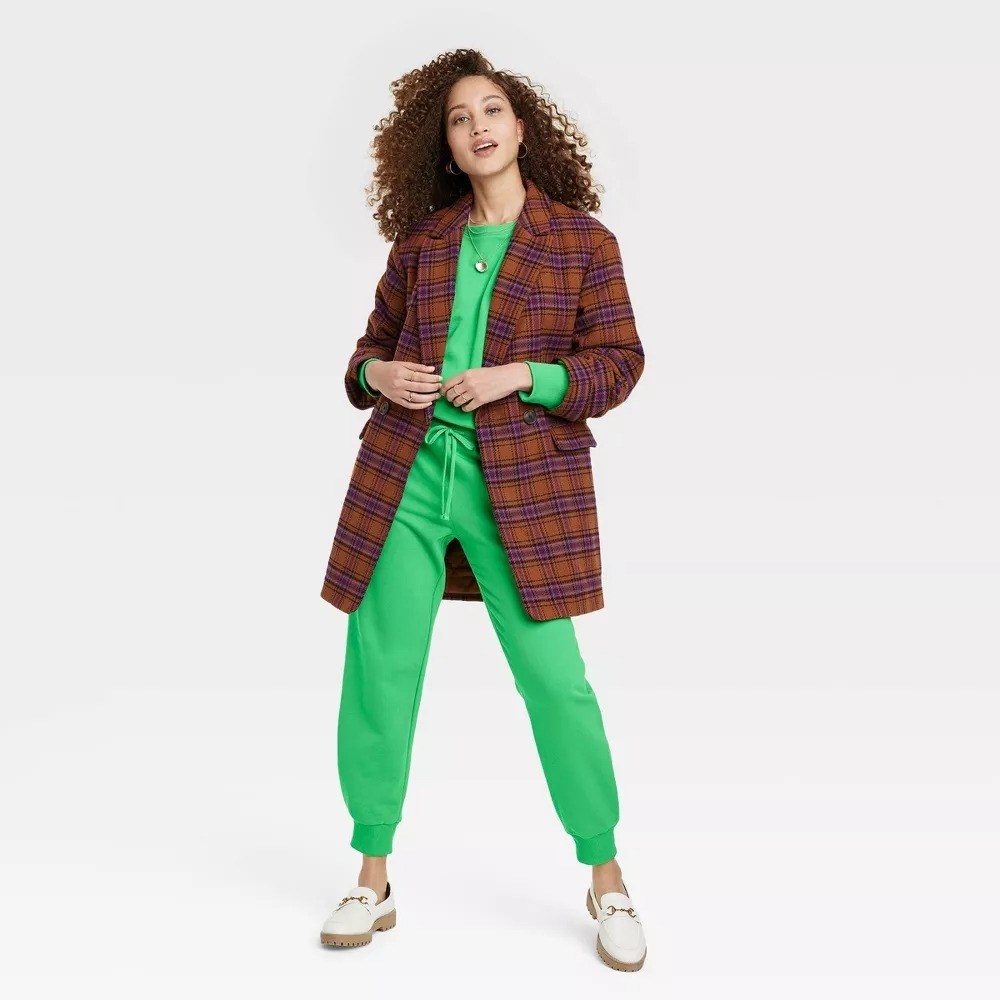 A model wearing the matching bright sweatpants and a sweatshirt with a brown plaid coat over it