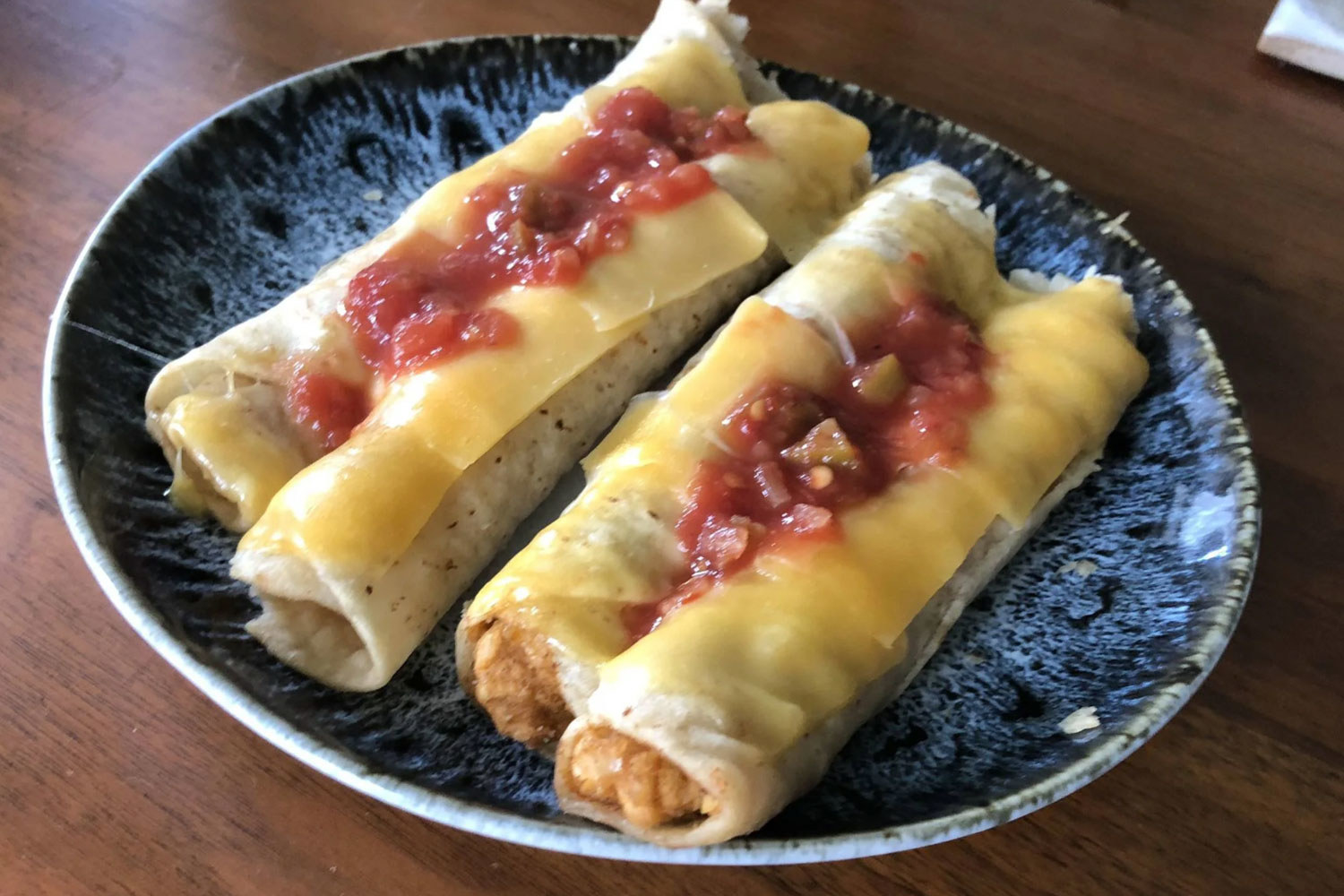Taquitos topped with melted cheese and salsa