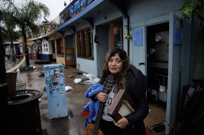 A distressed woman carries musical instruments out of a flooded restaurant onto the street