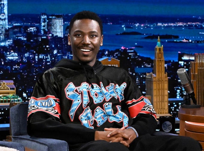 Jerrod smiles as he looks at the audience while being interviewed on a late-night TV show