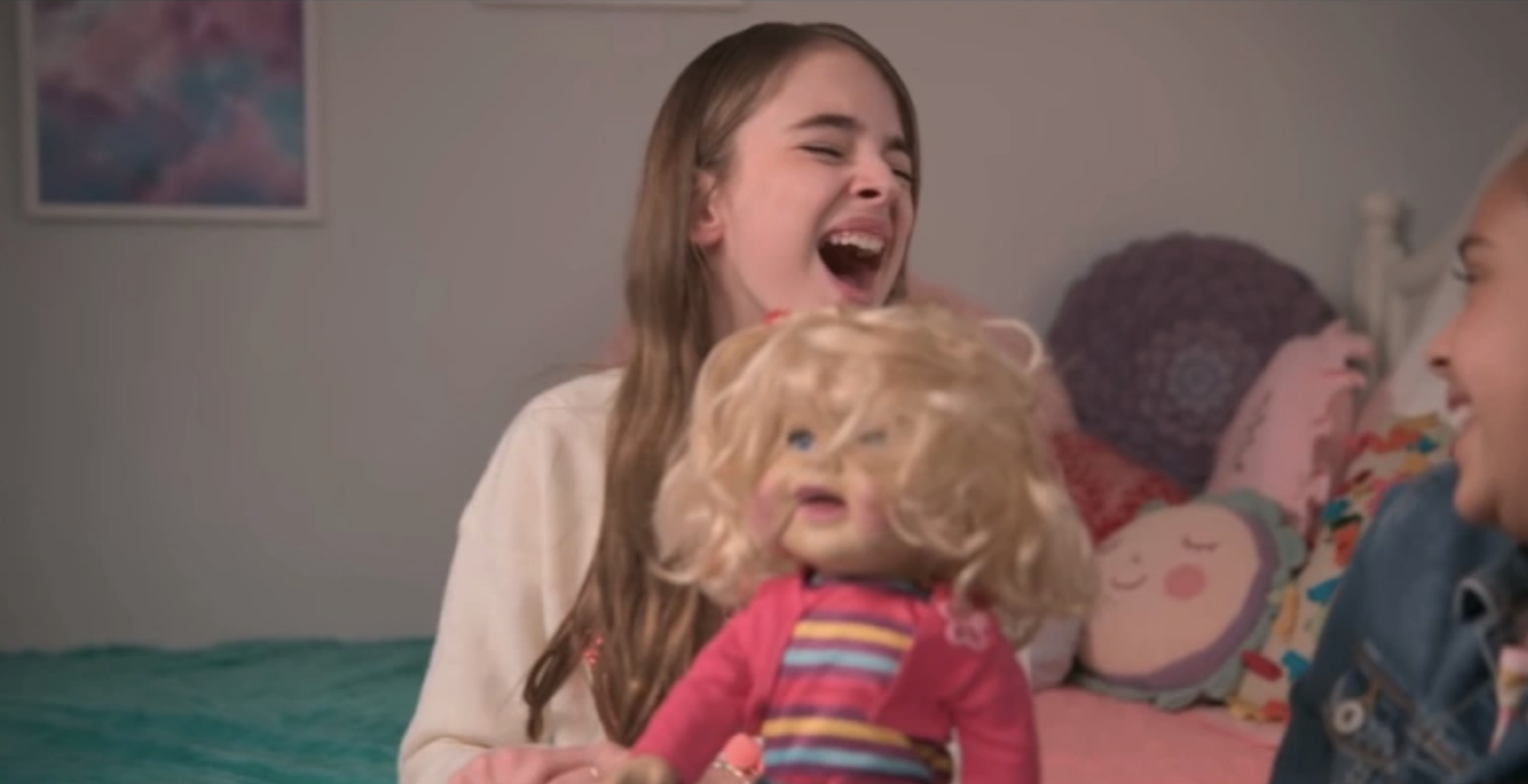 a young girl with long hair holds a doll with curly hair. the girl laughs maniacally.