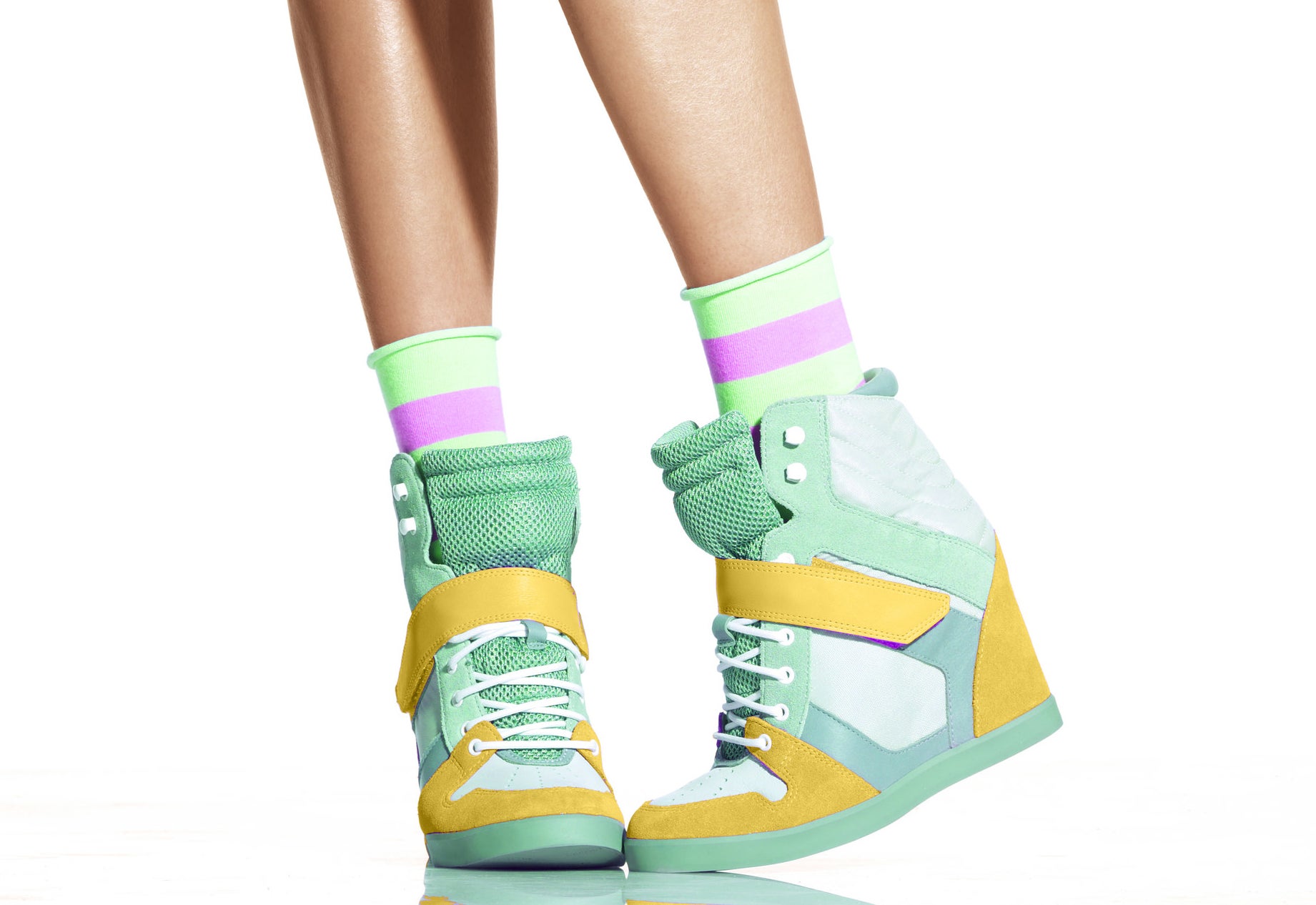 A shot of a model from waist down, showing green and yellow high wedge sneakers
