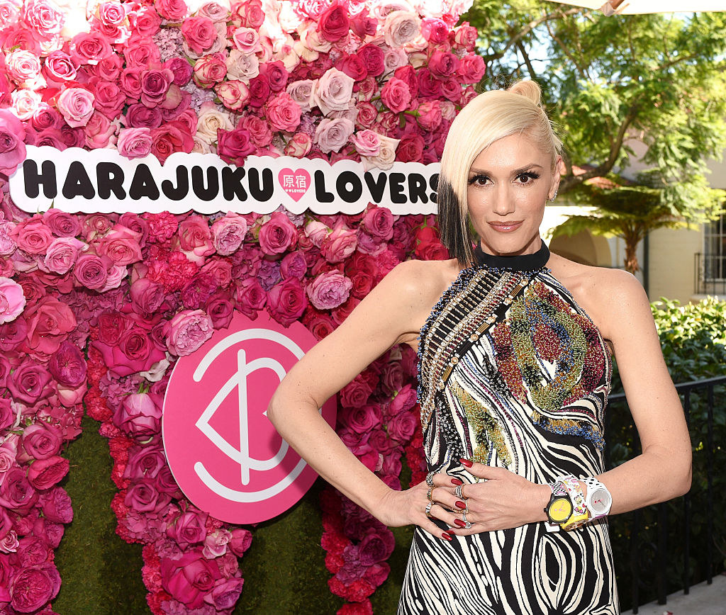 Gwen standing next to a flower wall with an attached sign that says &quot;Harajuku Lovers&quot;