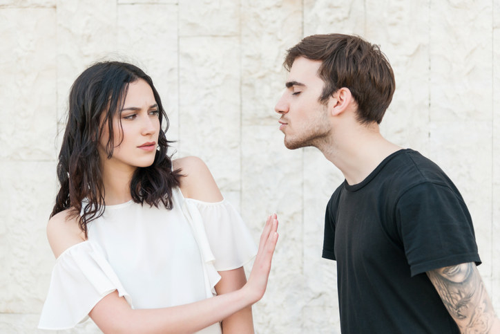 A young woman holding her hand out to a guy trying to kiss her