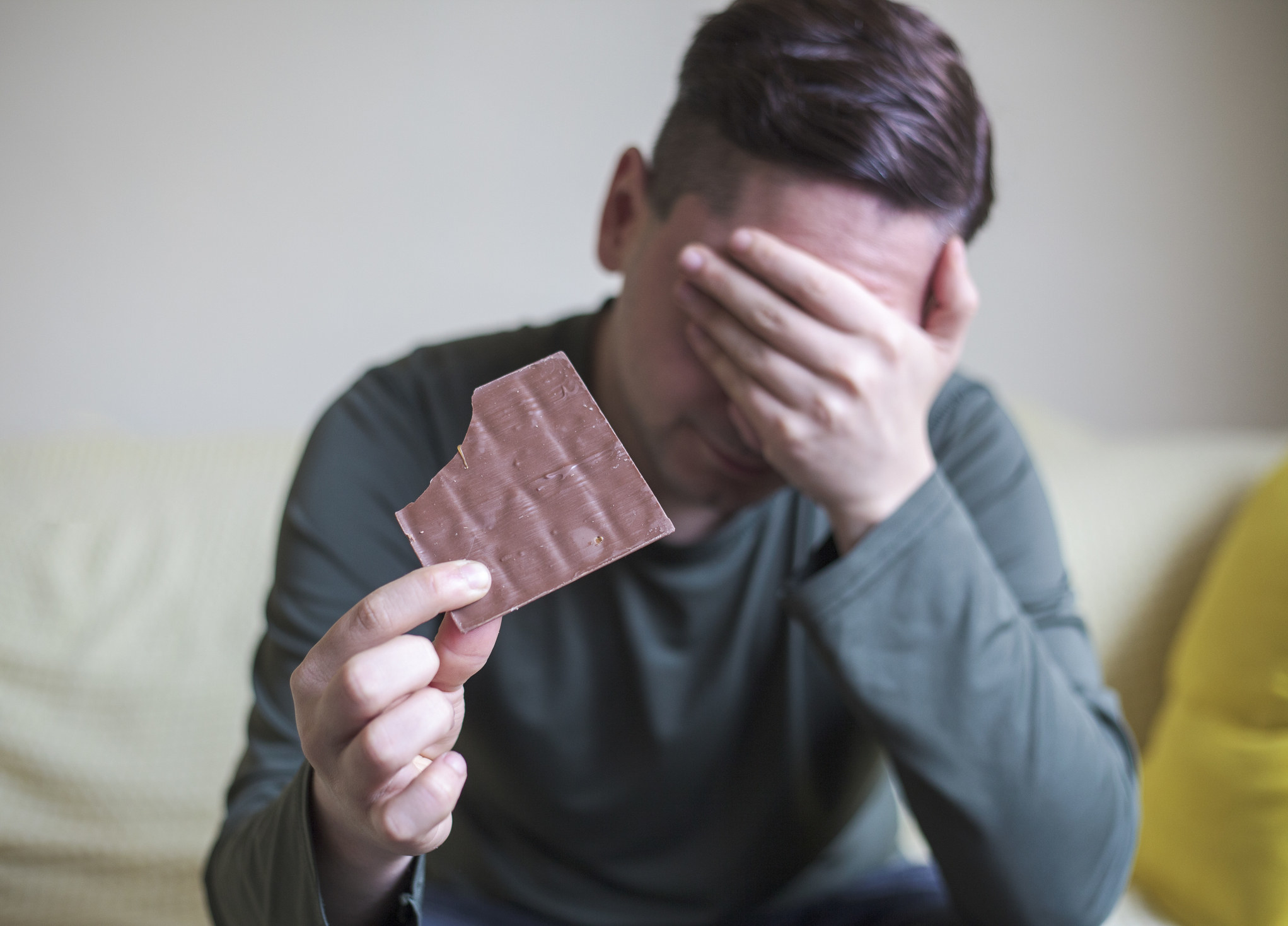 A man eating chocolate with his head in his hands